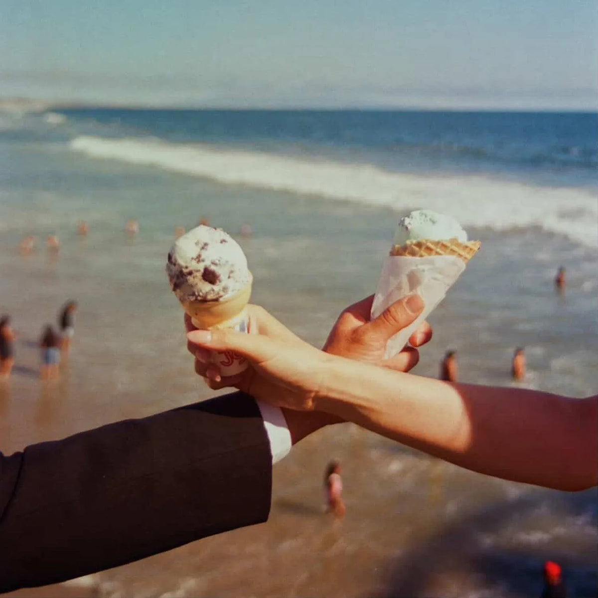 Two ice cream cones held by people on a beach with ocean and people in the background Pentax 17 Film Camera.