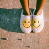 photograph of A person wearing fluffy white slip-on slippers with a yellow smiley face on the front, standing on a sandy ground outdoors taken with the Yashica T4 35mm Film Camera