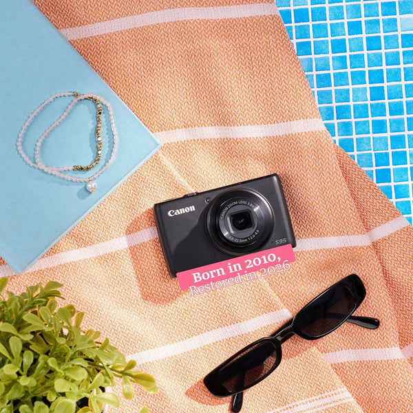 Restored Canon PowerShot S95 styled with poolside accessories, labeled Born in 2010, Restored in 2026