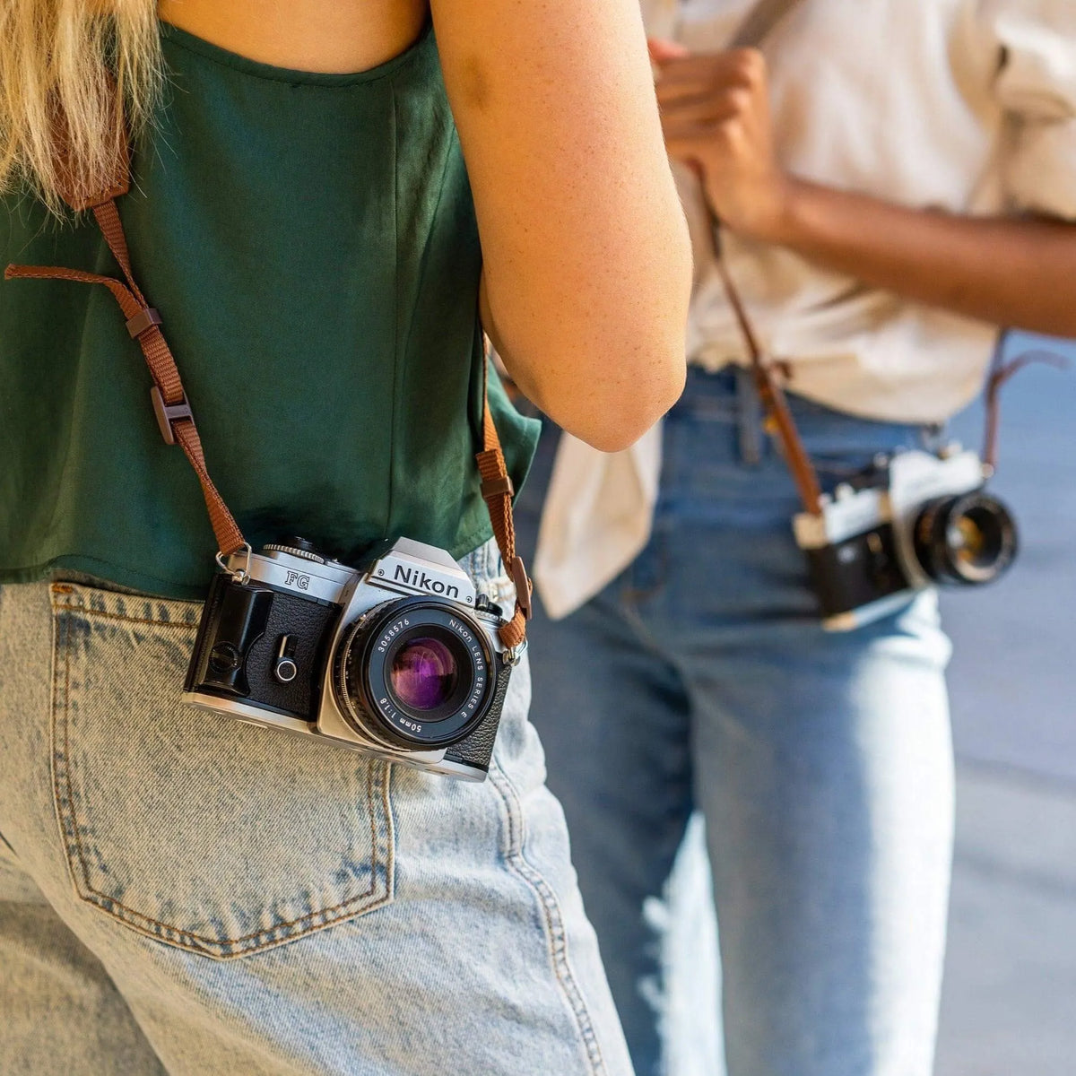 Two people with Nikon FG SLR film cameras around their necks, one wearing a green shirt and blue jeans.