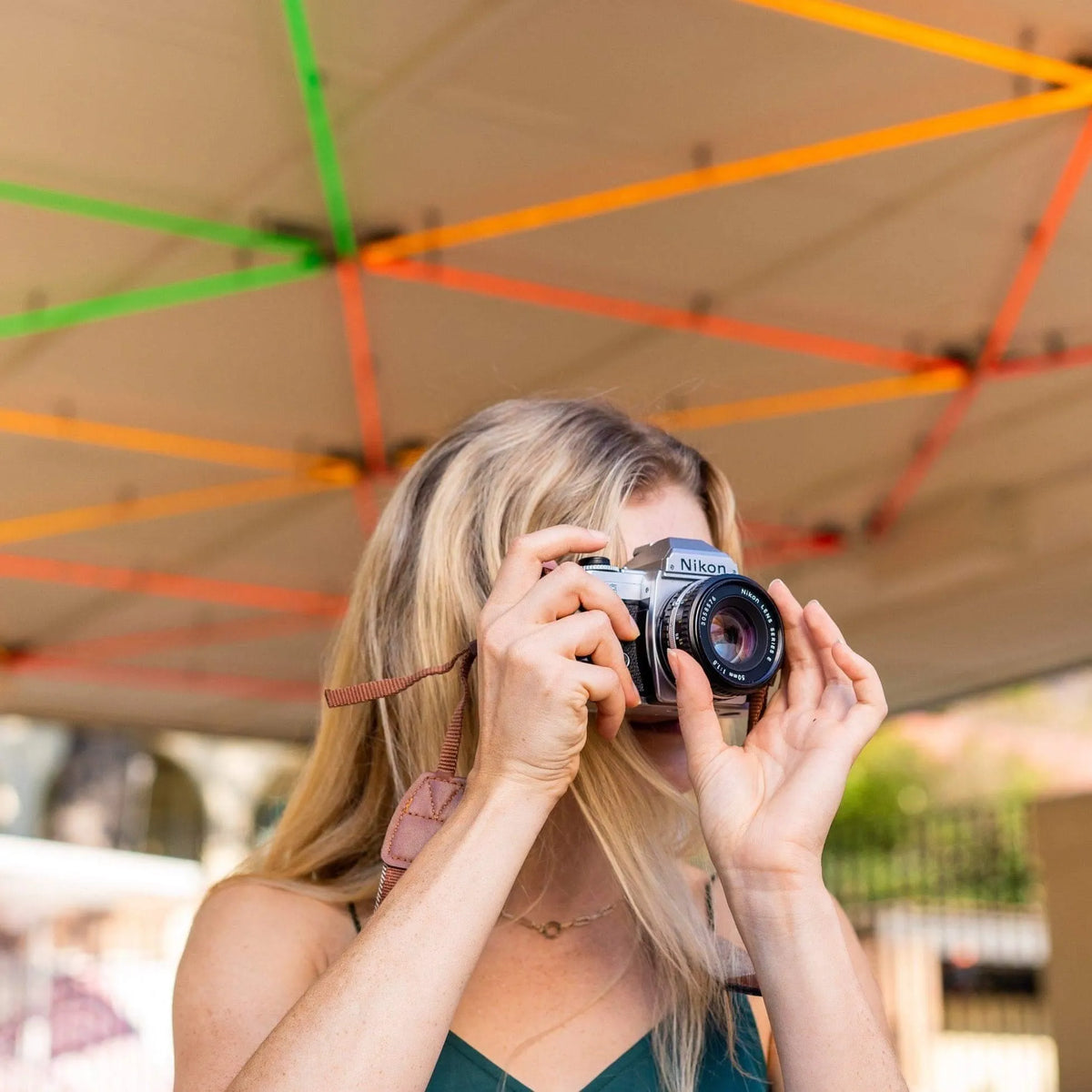 Person holding a Nikon FG SLR film camera under a colorful canopy