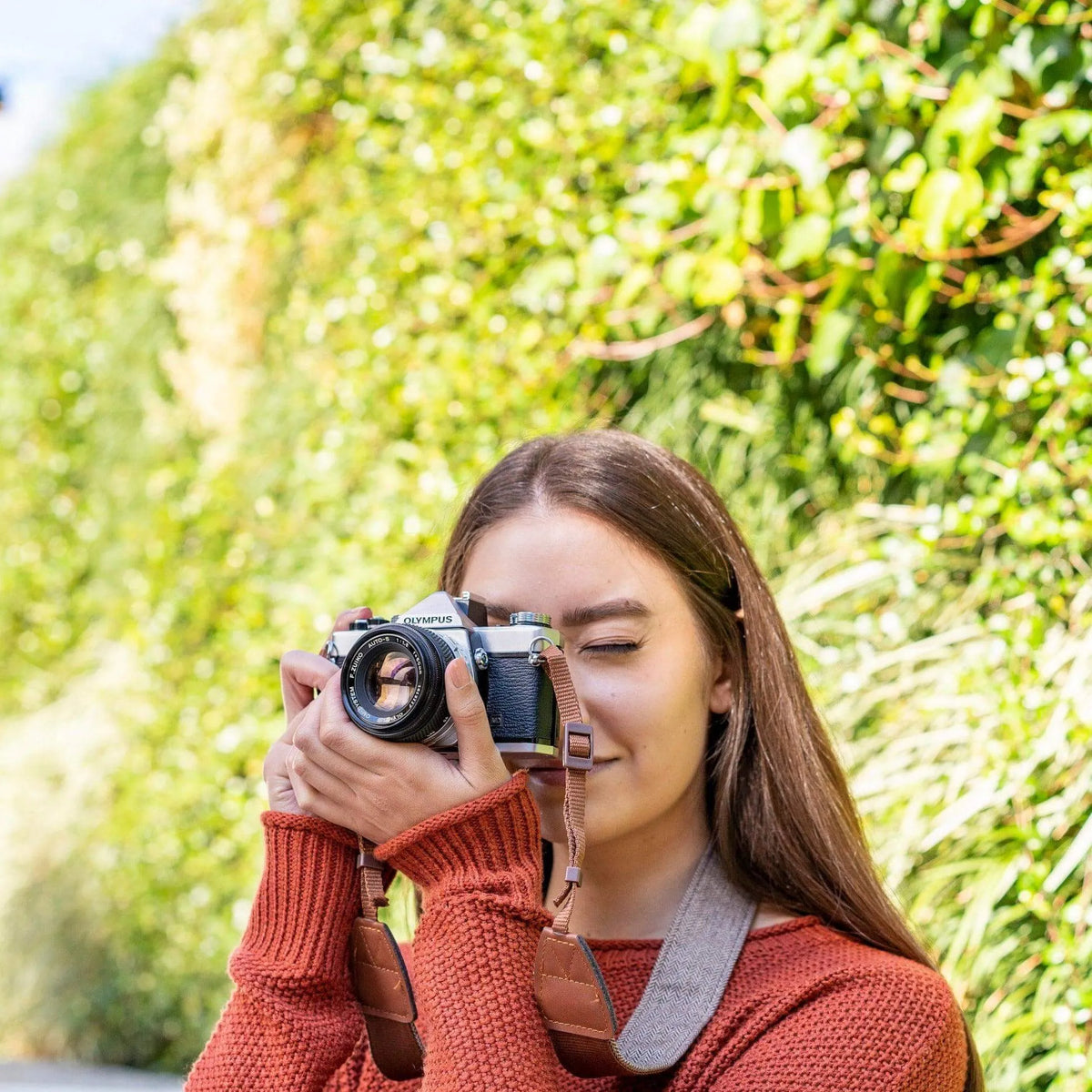 Woman holding a Olympus OM-1 | 35mm Film Camera with a blurred green background