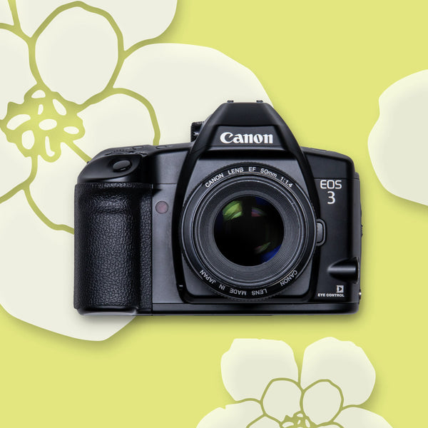 A Canon EOS 3 35mm film camera with an EF 50mm F1.4 Lens, displayed against a yellow background with white floral designs.